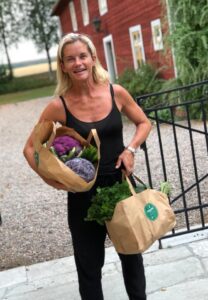 Leende kvinna med papperspåsar fyllda med grönsaker