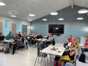 en grupp åhörare sitter kring små bord i föreläsningssal