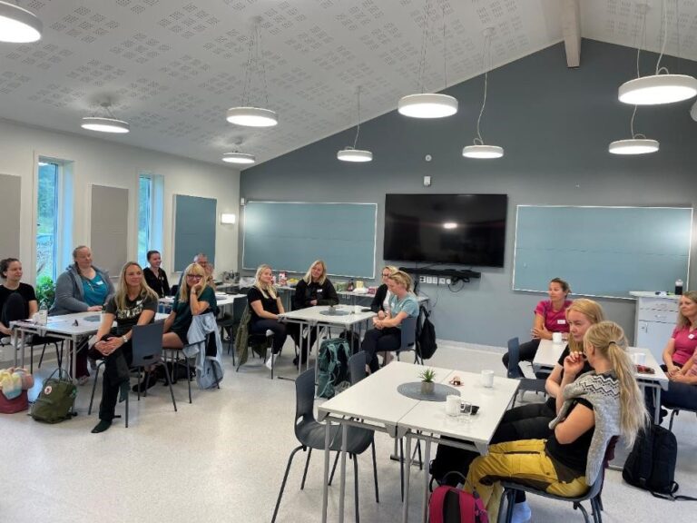 en grupp åhörare sitter kring små bord i föreläsningssal