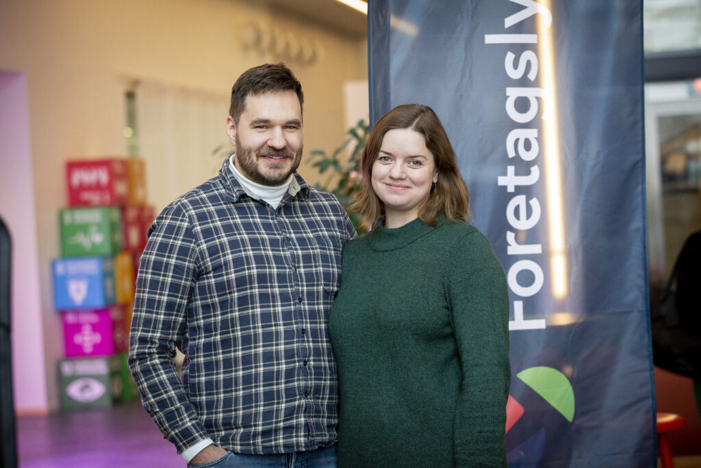 En man och en kvinna står framför en mörkblå beachflagga. i bakgrunden syns agenda 2030 kuber i olika färger.