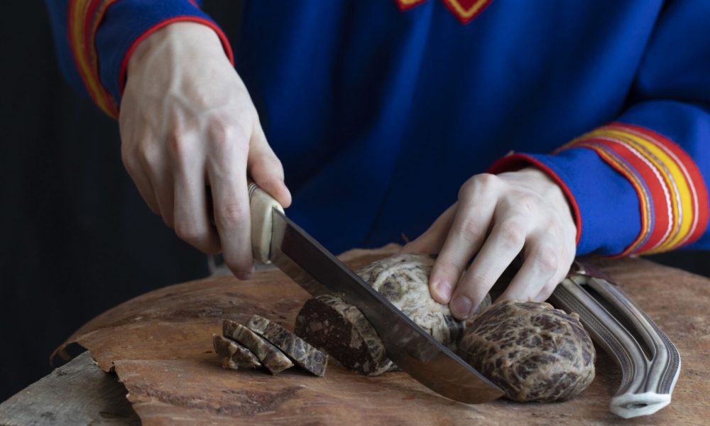 Person i samiska kläder som skär upp renkött