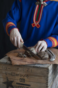 Person i samiska kläder som skär upp renkött