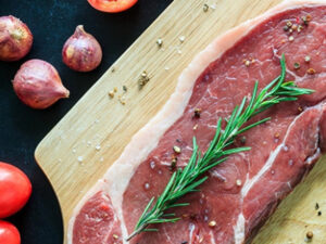 Rå köttbit på planka med rosmarin, lök och tomat