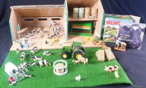 Ett foto på undervisningmaterial bestående av en bondgård i miniatyr byggd i trä, leksaksdjur, böcker om lantbruk, en grön leksakstraktor.