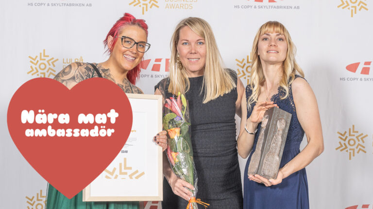 Tre unga kvinnor håller fram ett diplom och blombukett