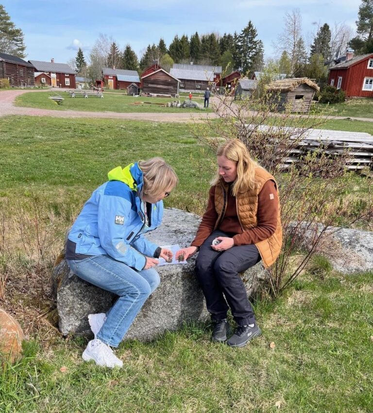 två lärare sitter på en sten i skolträdgård